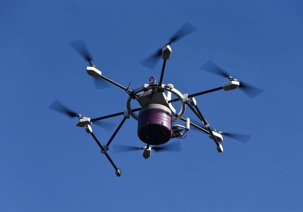 A purple and white drone flying in the sky.